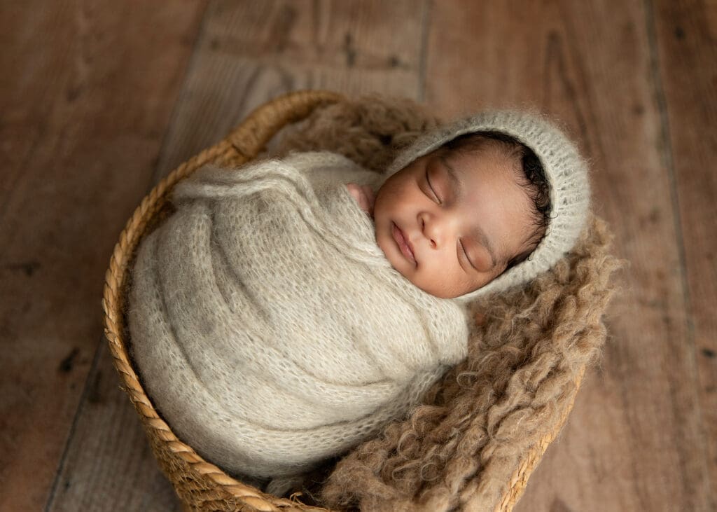 newborn boy wrapped with a bonnet posing in basket in Tulsa studio