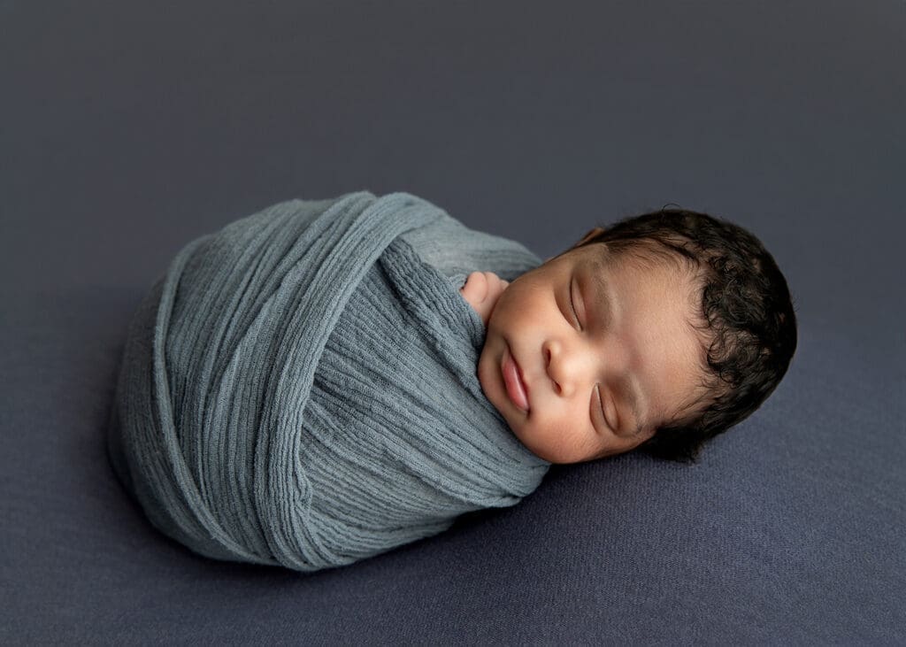baby boy in blue swaddled and sleeping in newborn studio Tulsa